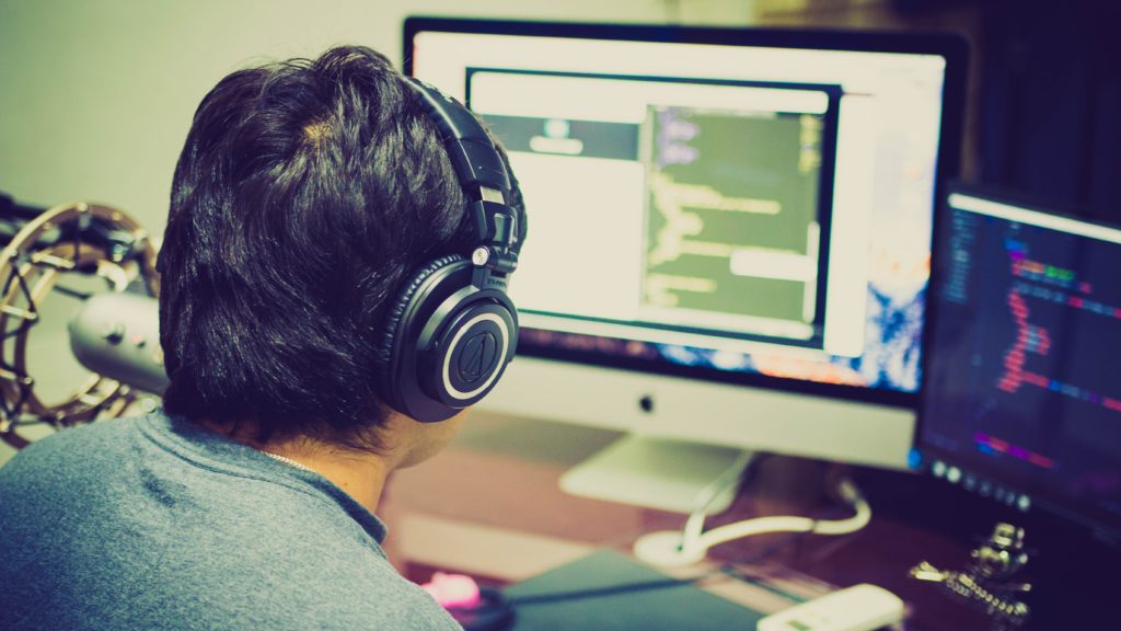 Back view of a man sitting at this laptop with headphones on