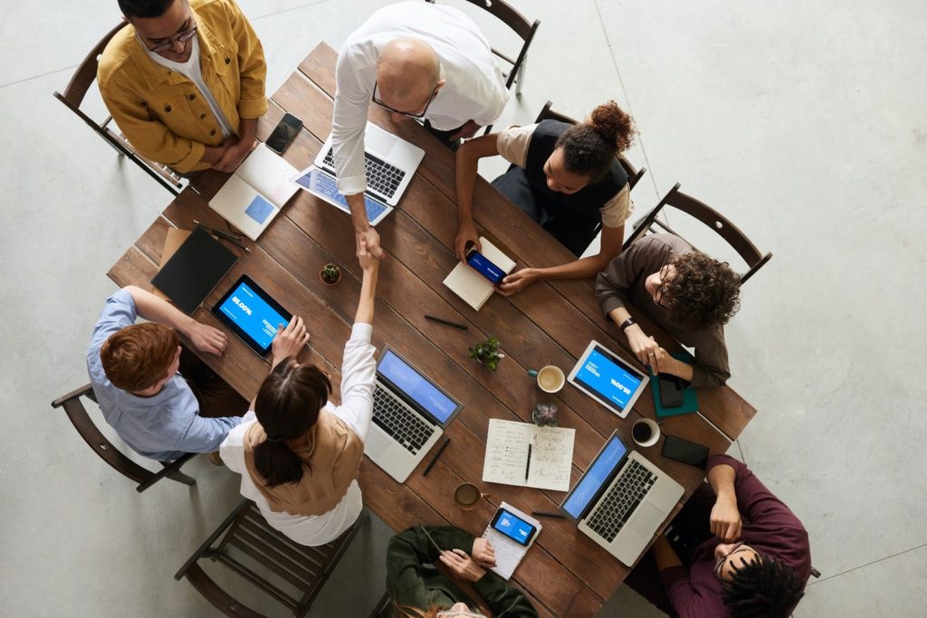 A group of professionals at a meeting table with a variety of devices open in front of them