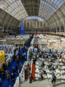 An aerial view of the main hall of the london book fair taken from the 1st floor mezzanine. The fair looks very busy with lots of stands in shot