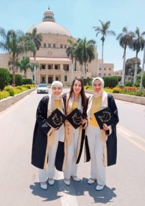 The three students wearing their graduation caps and gowns standing Infront of the Cairo University Dome Building.