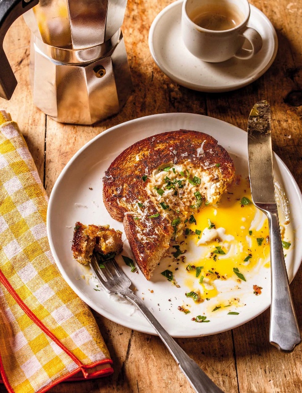 A plate with a piece of fried egg in toast next to a fork and knife, with a coffee maker and a cup in the background